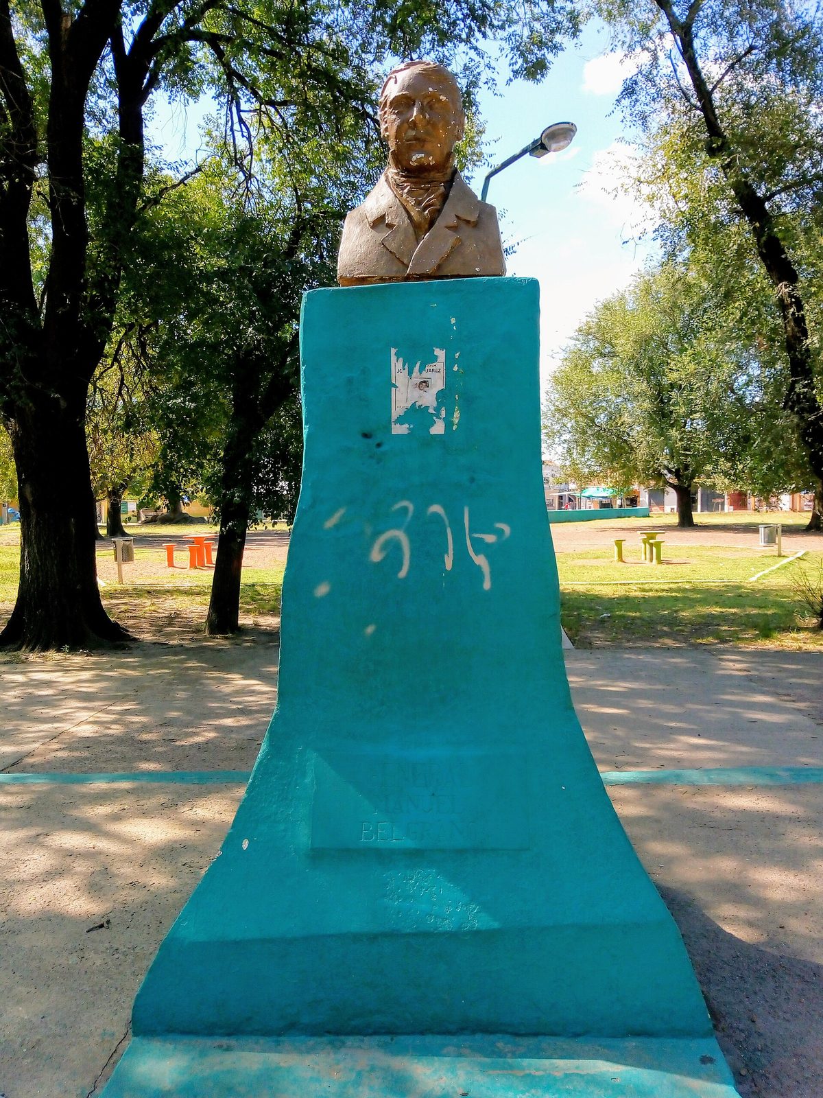 Busto de Manuel Belgrano sobre un pedestal turquesa en la plaza de Gobernador Costa