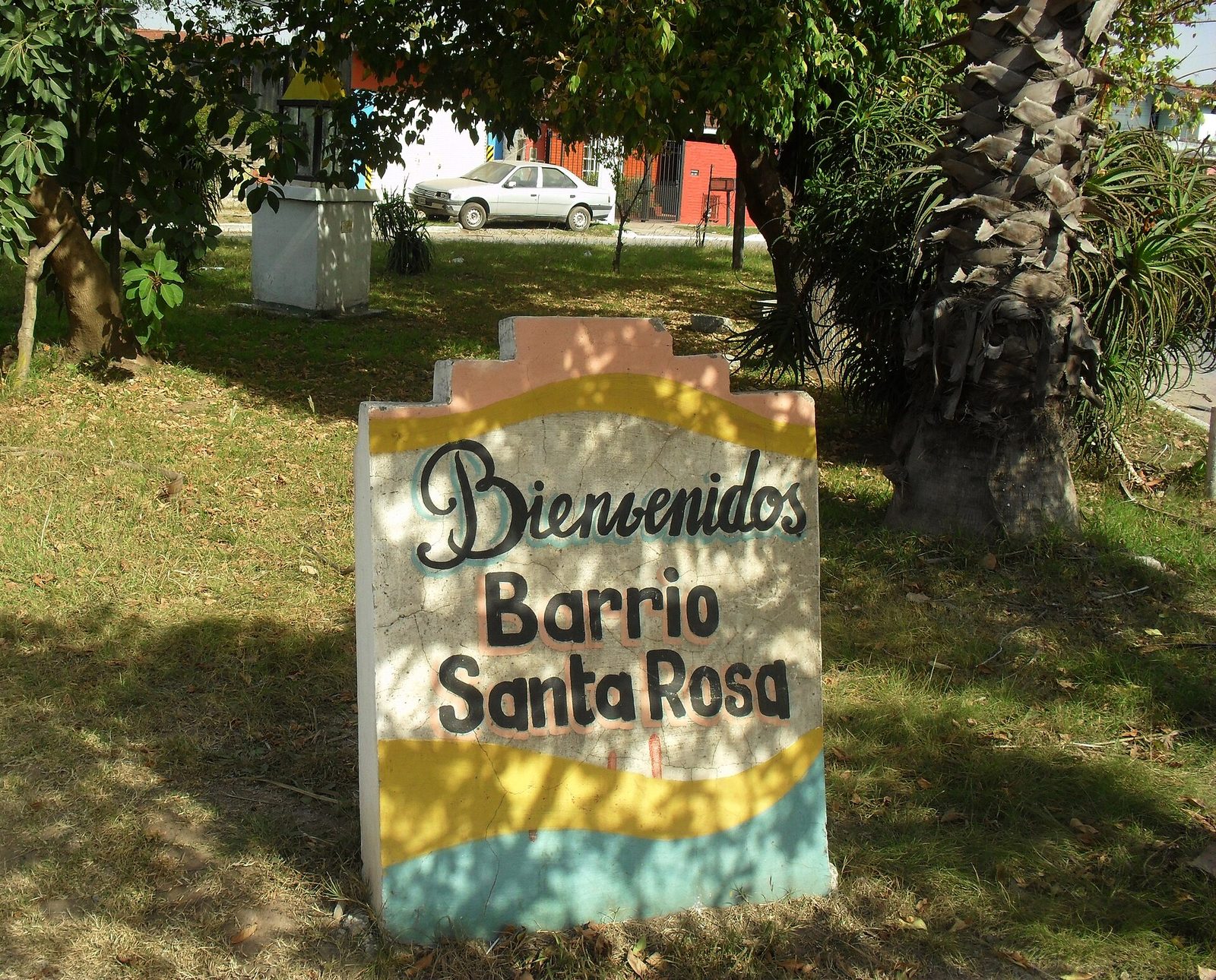 Cartel pintado a mano que da la bienvenida al barrio Santa Rosa entre árboles